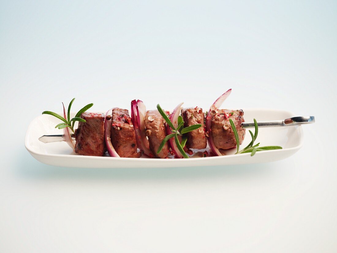 A lamb kebab on a plate against a white background