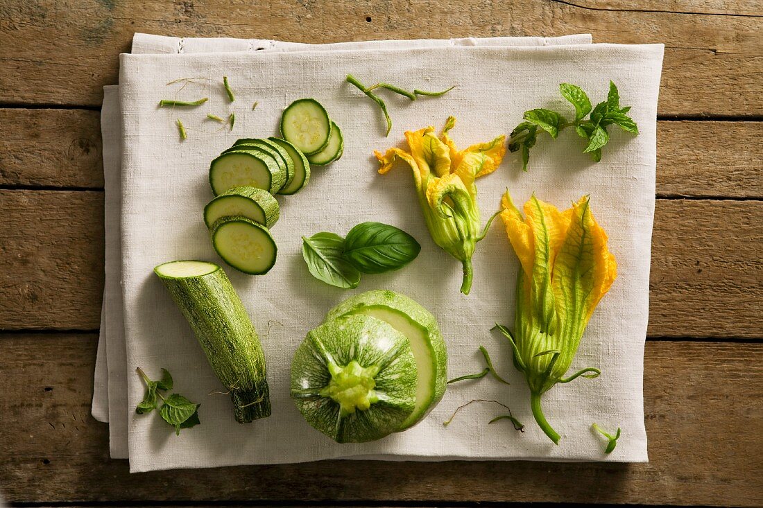 A still life featuring courgettes, courgette flowers and herbs