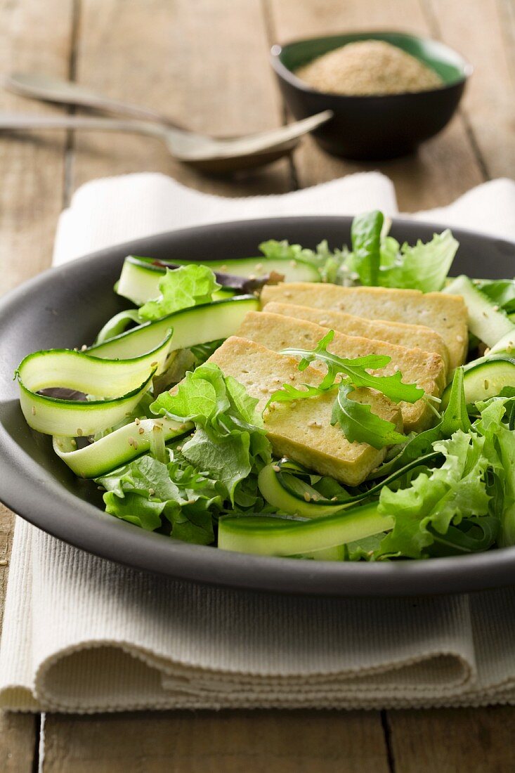 Fried tofu on a bed of salad with courgette strips