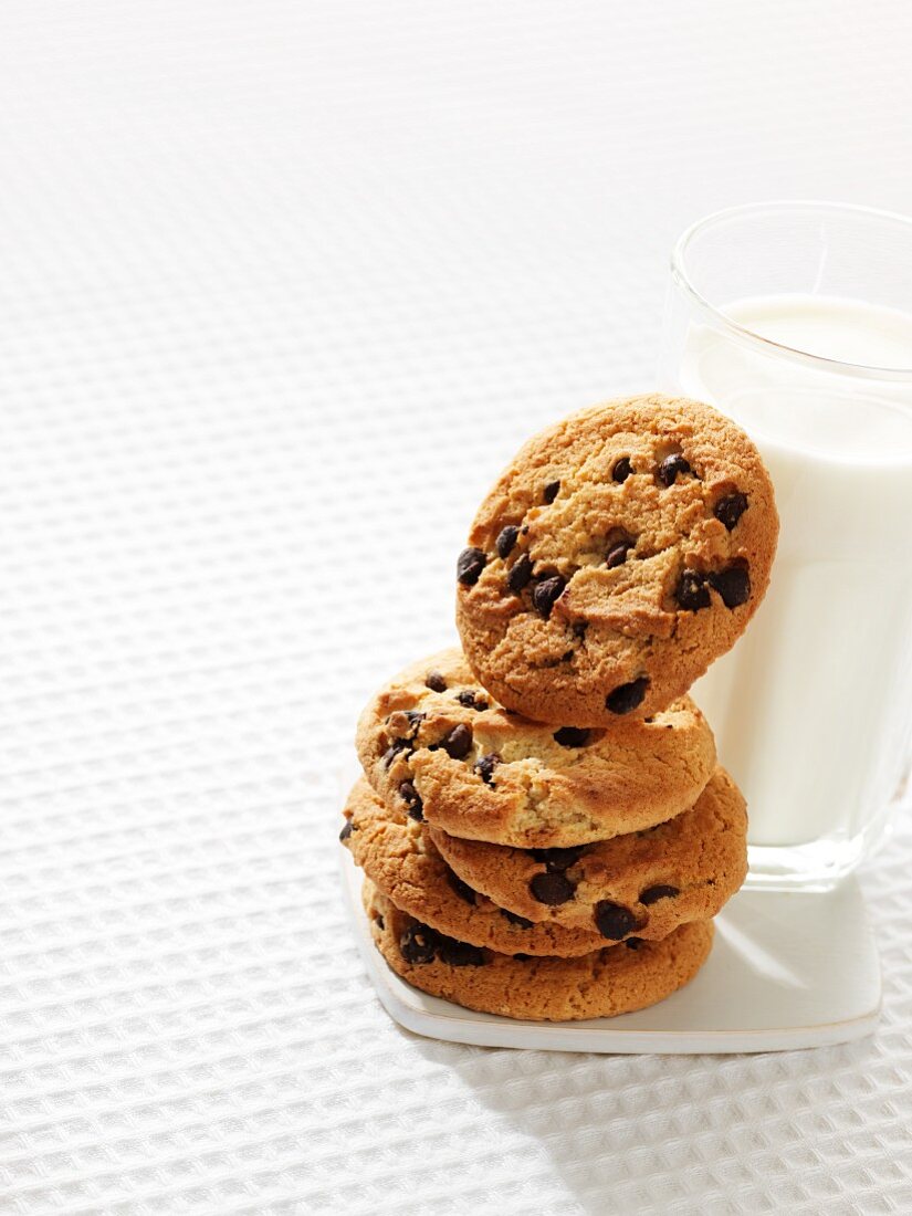 A stack of chocolate chip cookies next to a glass of milk