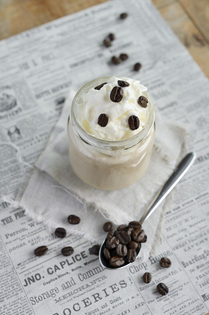 Latte topped with whipped cream in a screw-top jar, and coffee beans