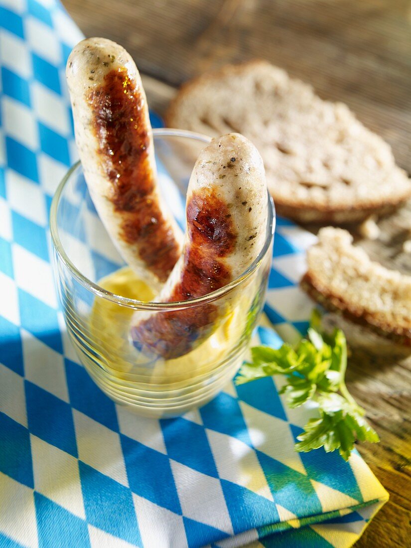 Two grilled bratwurst sausages in a glass with mustard
