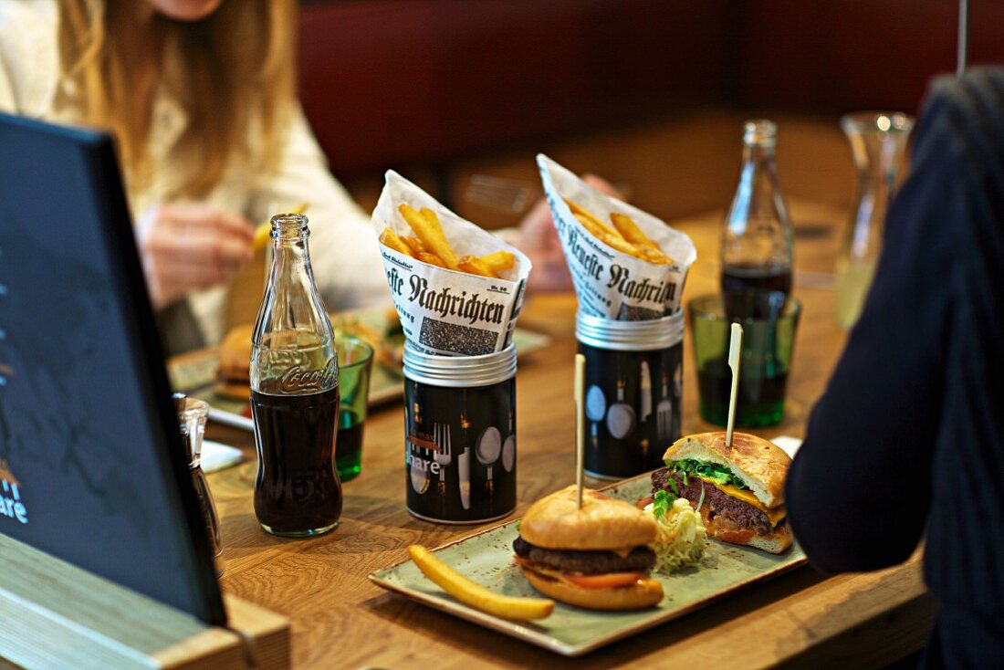 Two young woman eating burgers with chips and drinking cola