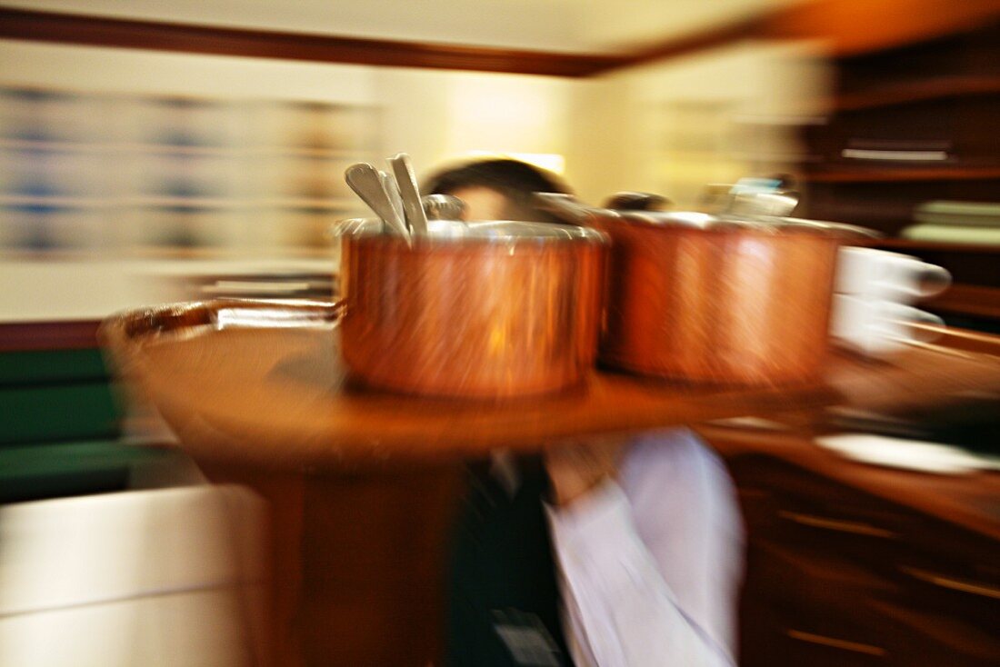 A waiter carrying a tray of copper pots