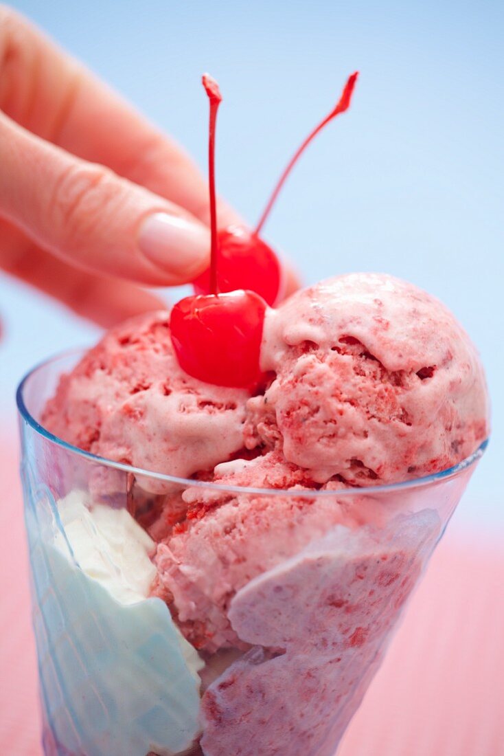 Strawberry ice cream being decorated with cocktail cherries