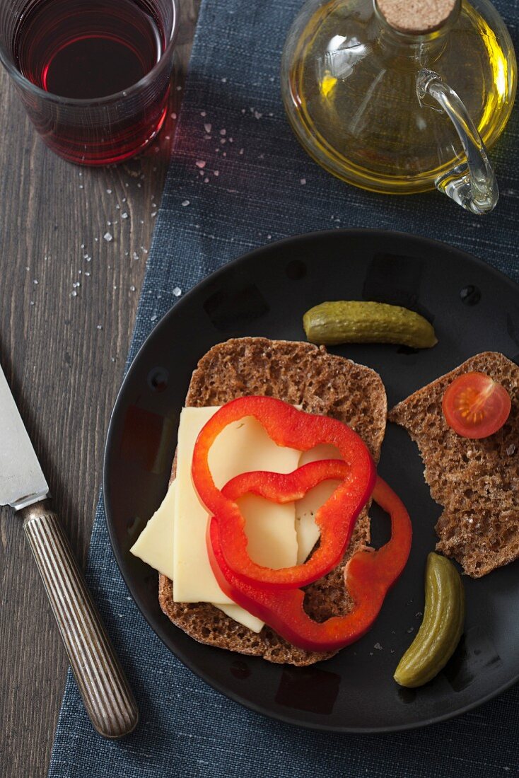 A slice of bread topped with cheese and peppers, with gherkins