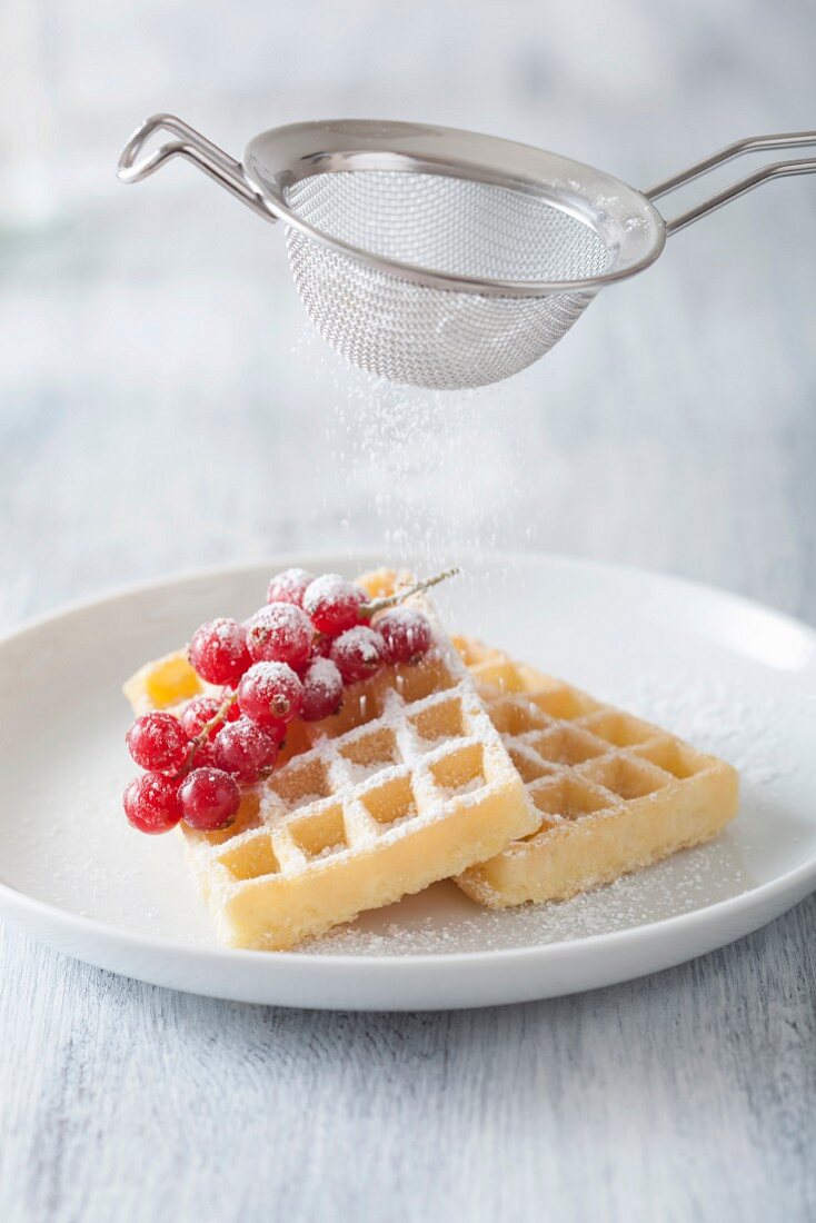 Waffles with redcurrants being dusted with sugar