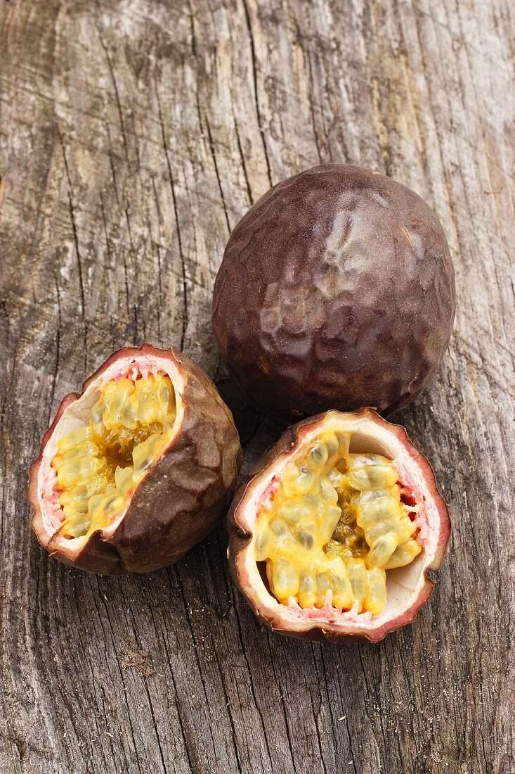 Red passion fruit, whole and halved, on a wooden surface