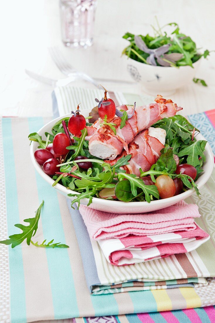 Chicken fillet wrapped in bacon on a bed of rocket with grapes
