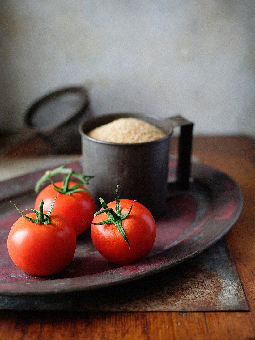 Frische Tomaten; im Hintergrund ein Metallbecher mit Couscous