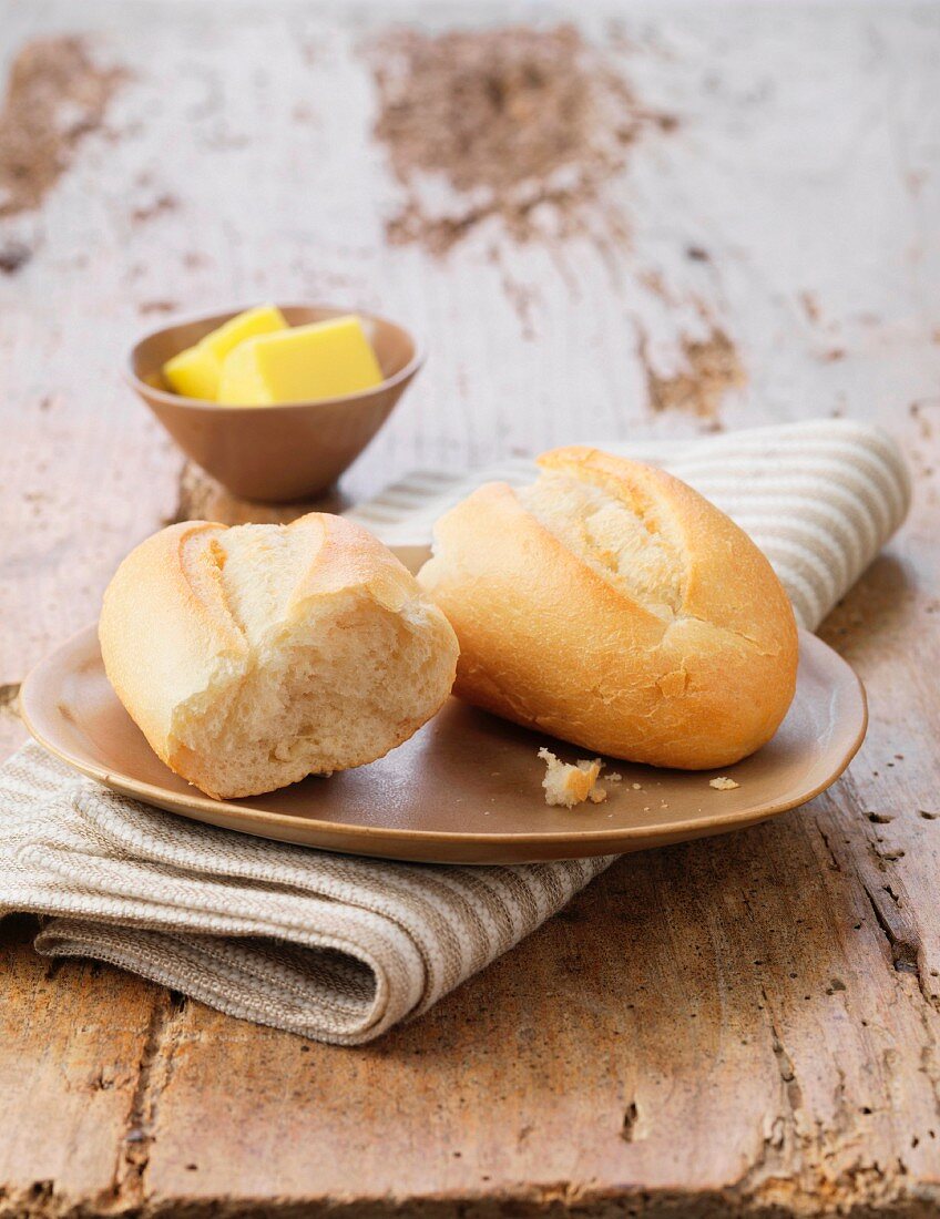 White petit pain with butter on ceramic plate and striped napkin