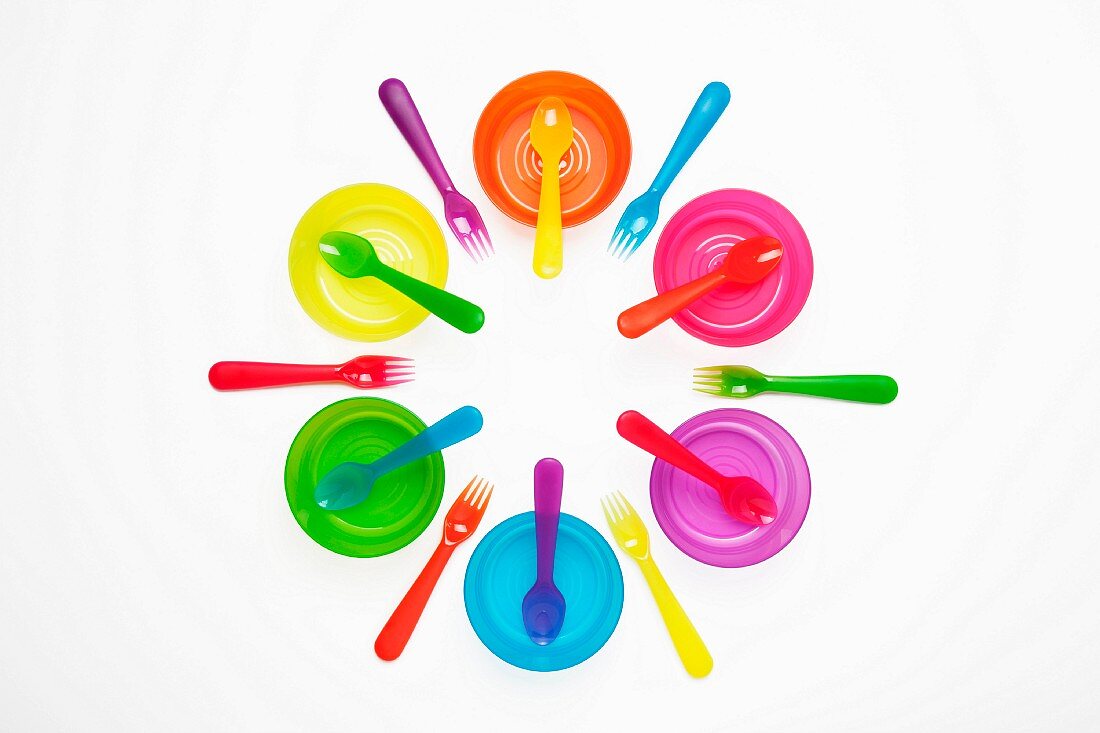 Colourful plastic plates, cups, bowls, spoons and forks