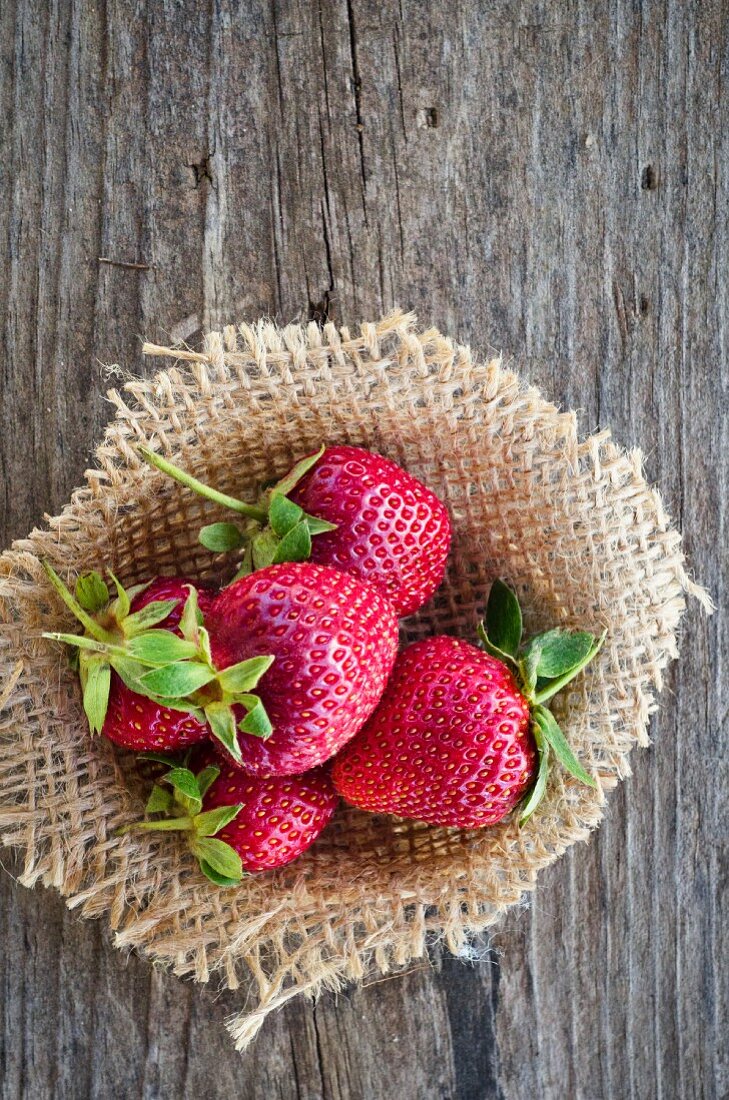 Fresh strawberries on sackcloth on a wooden surface (view from above)
