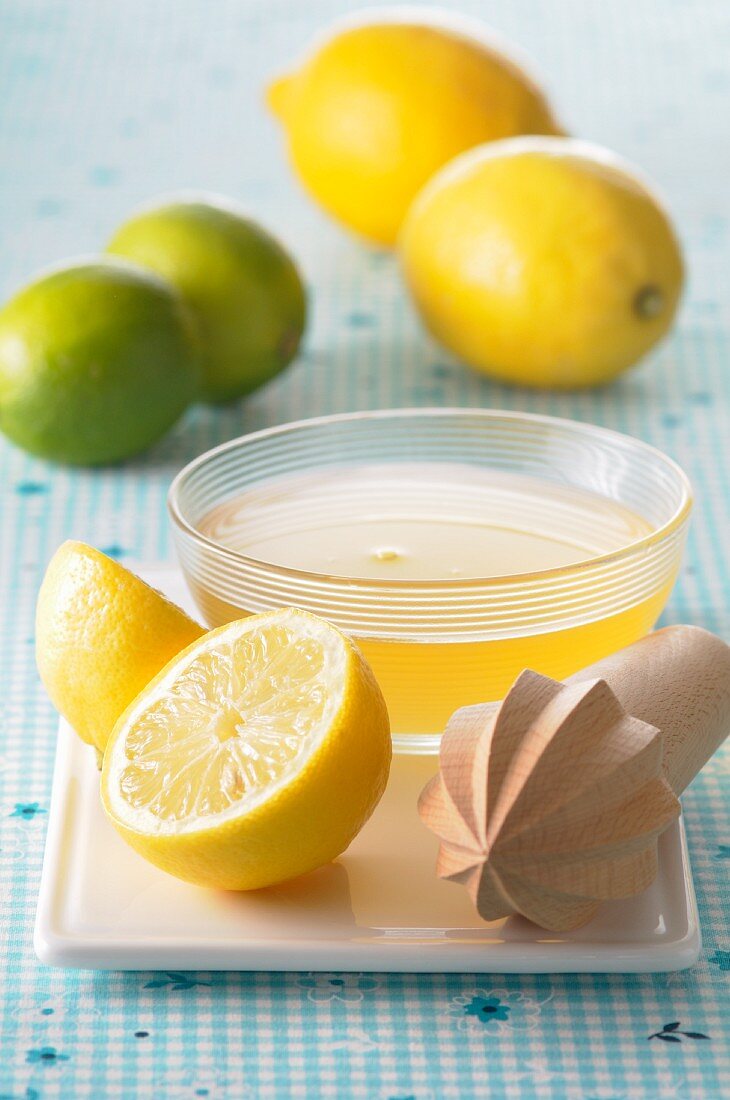 Lemon juice in a small dish, a lemon squeezer and citrus fruit