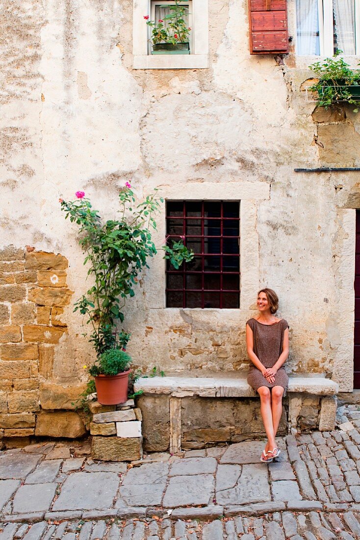 A woman sitting on a stone bench outside a house in Istria, Croatia