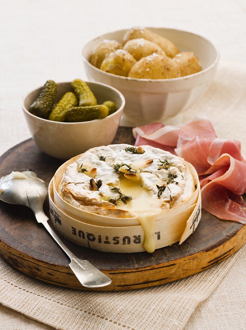 Baked soft cheese with potatoes, dry-cured ham and pickled gherkins