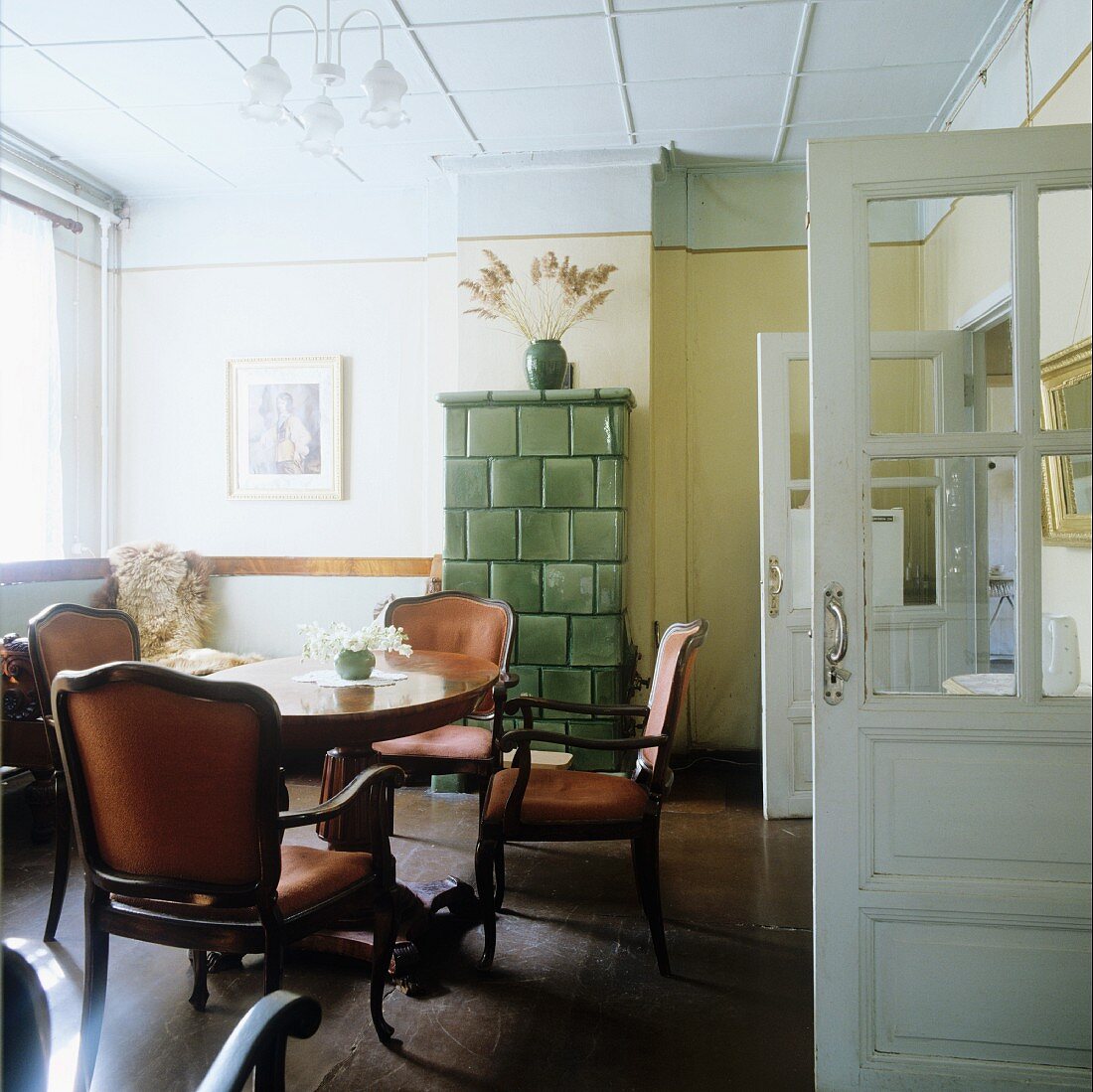 Antique armchairs at round table in front of corner bench and tiled stove in rustic, country-style room