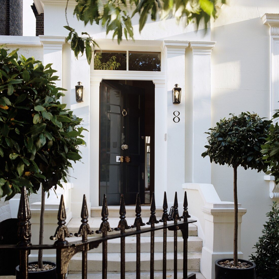 Wrought iron gate and small bay trees in front of traditional, English house