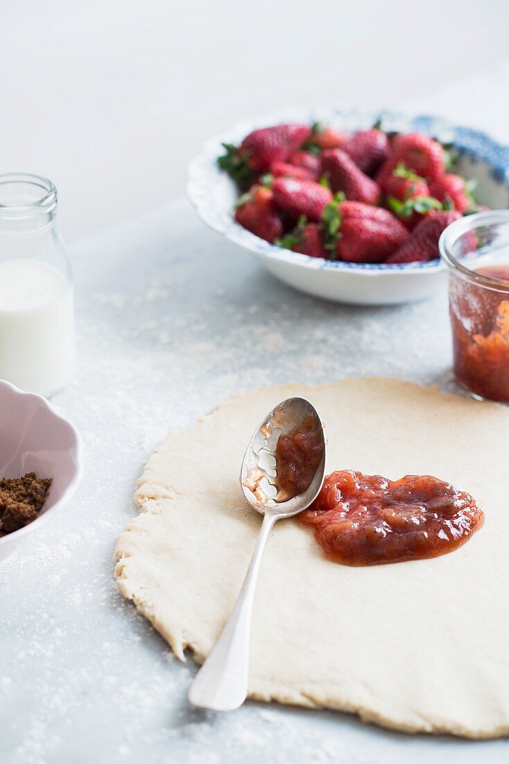 Einen Mürbteigboden mit Erdbeermarmelade bestreichen