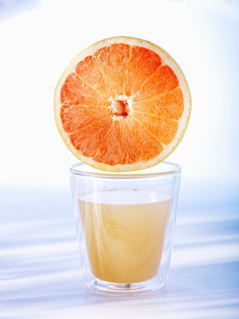 Half a grapefruit on top of a glass of grapefruit juice