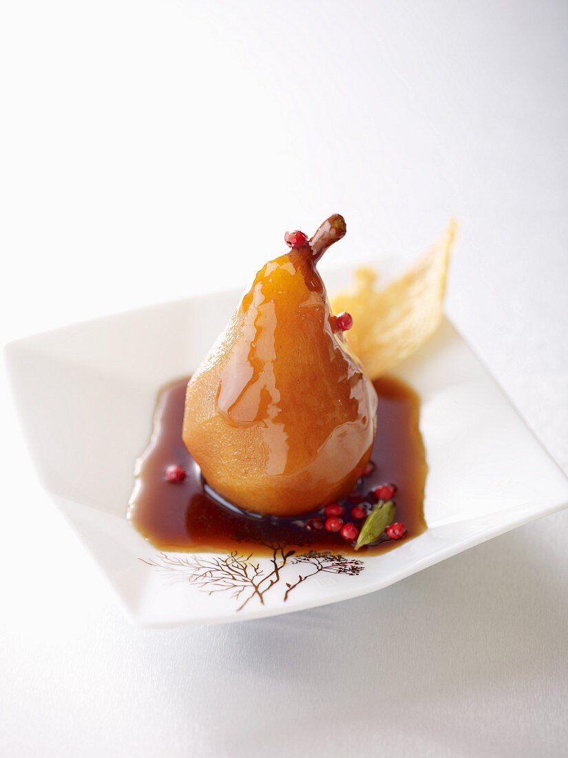 A poached pear in coffee syrup with red peppercorns