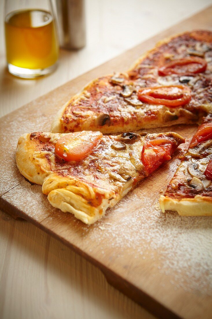 Pizza mit Salami, Tomaten und Champignons auf Holzbrett