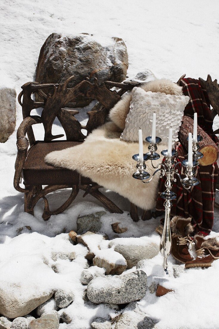 Holzbank mit Tierfell und Kissen und Kerzenständer im Schnee