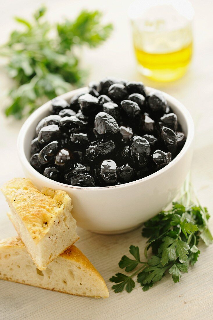 Schwarze Oliven in einer Schale mit Brot und Petersilie