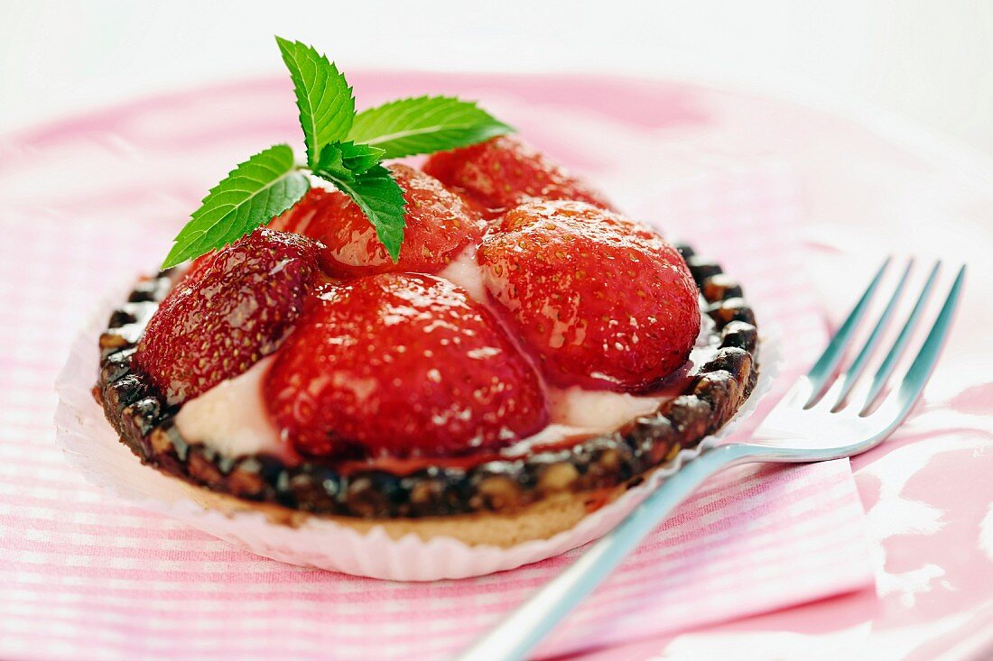 An individual strawberry tart with mint leaves