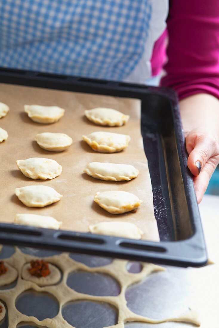 A woman holding a baking tray of uncooked pastry parcels, filled with lentils and tomatoes