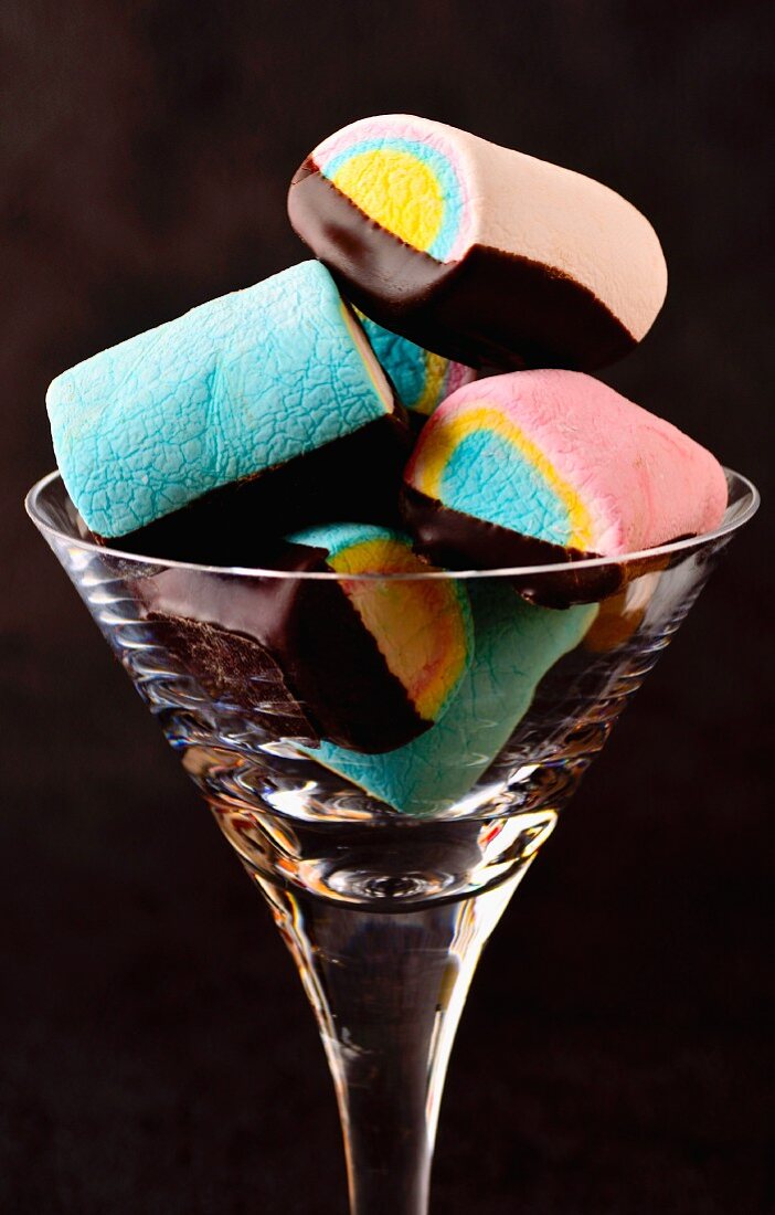 Colourful marshmallows with chocolate glaze in a glass against a black background