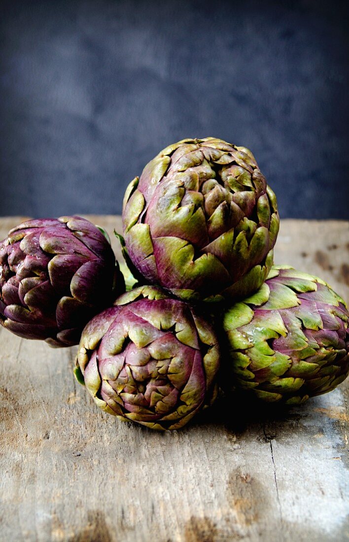 Four purple artichokes on a wooden surface