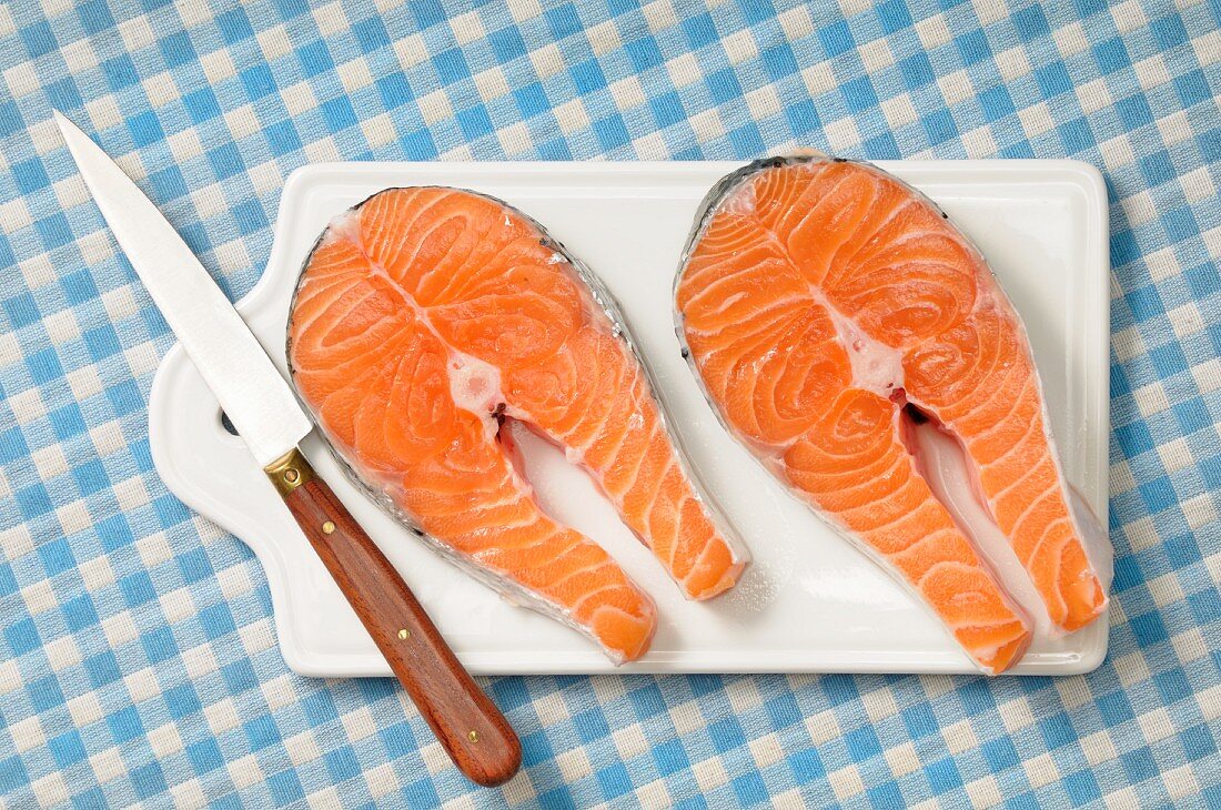 Two fresh salmon steaks on a chopping board with a knife