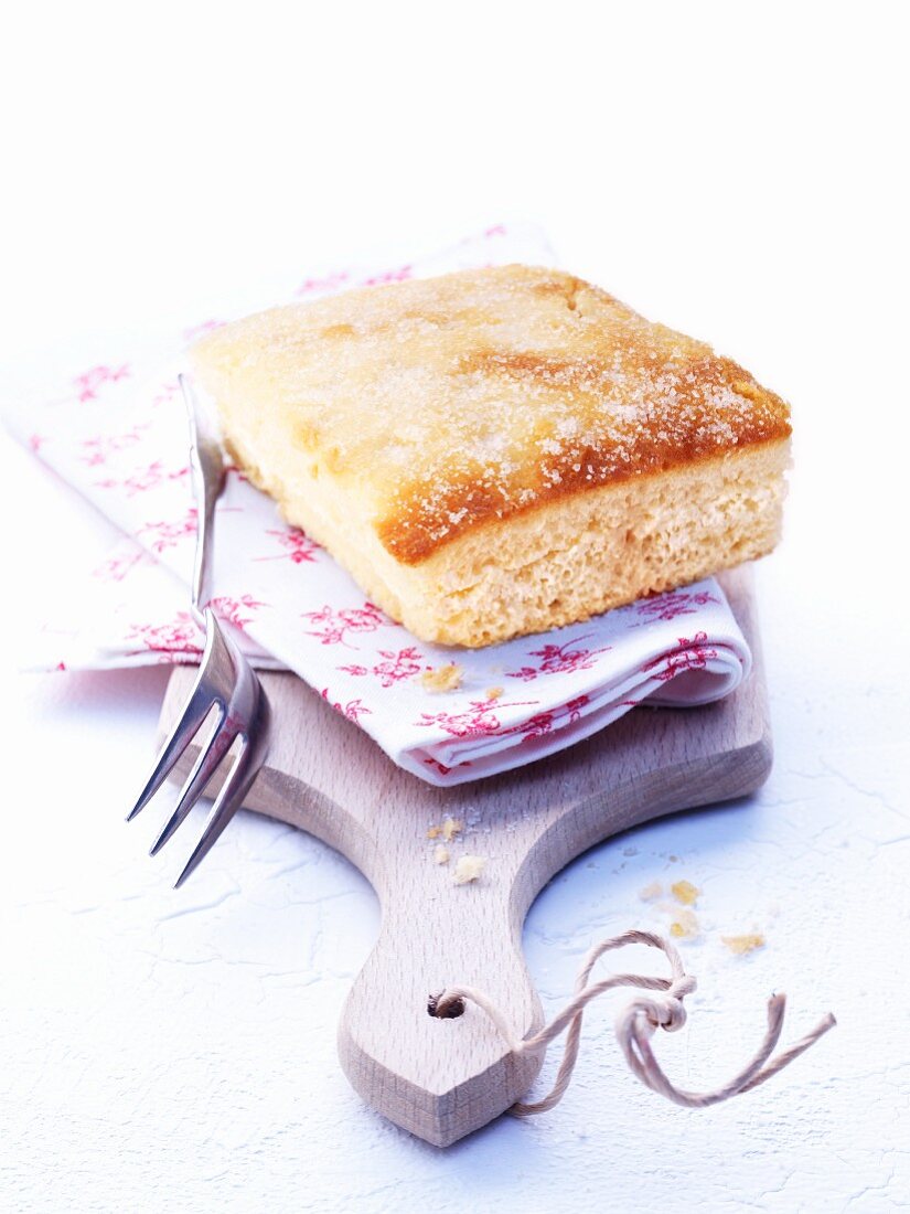 A piece of butter cake with a floral cloth on a chopping board