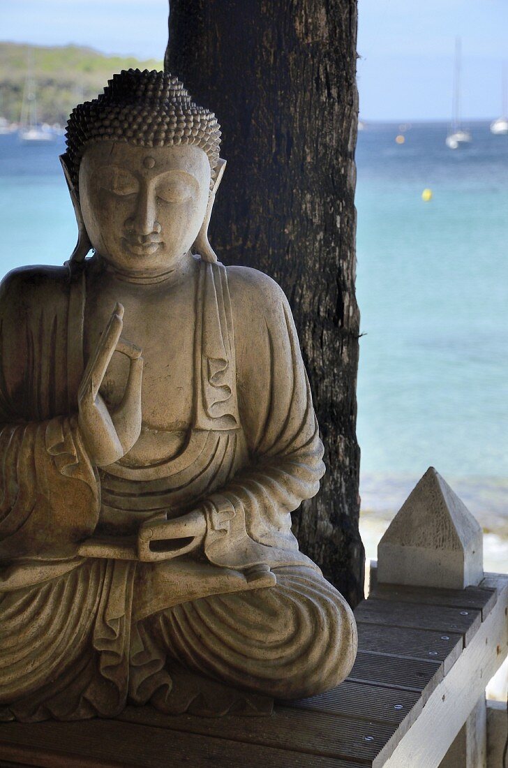 Stone Buddha statue on a wooden platform on the beach with an ocean view