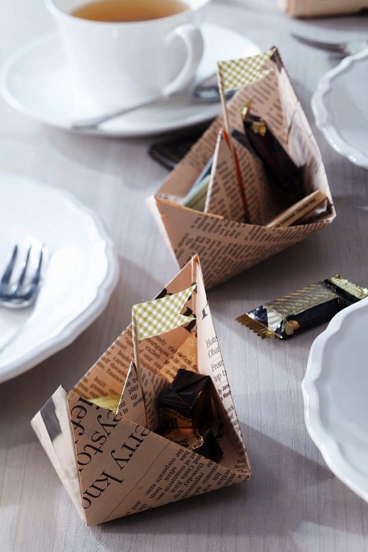 Papierschiffchen aus Zeitungspapier befüllt mit Schokolade als Tischdeko