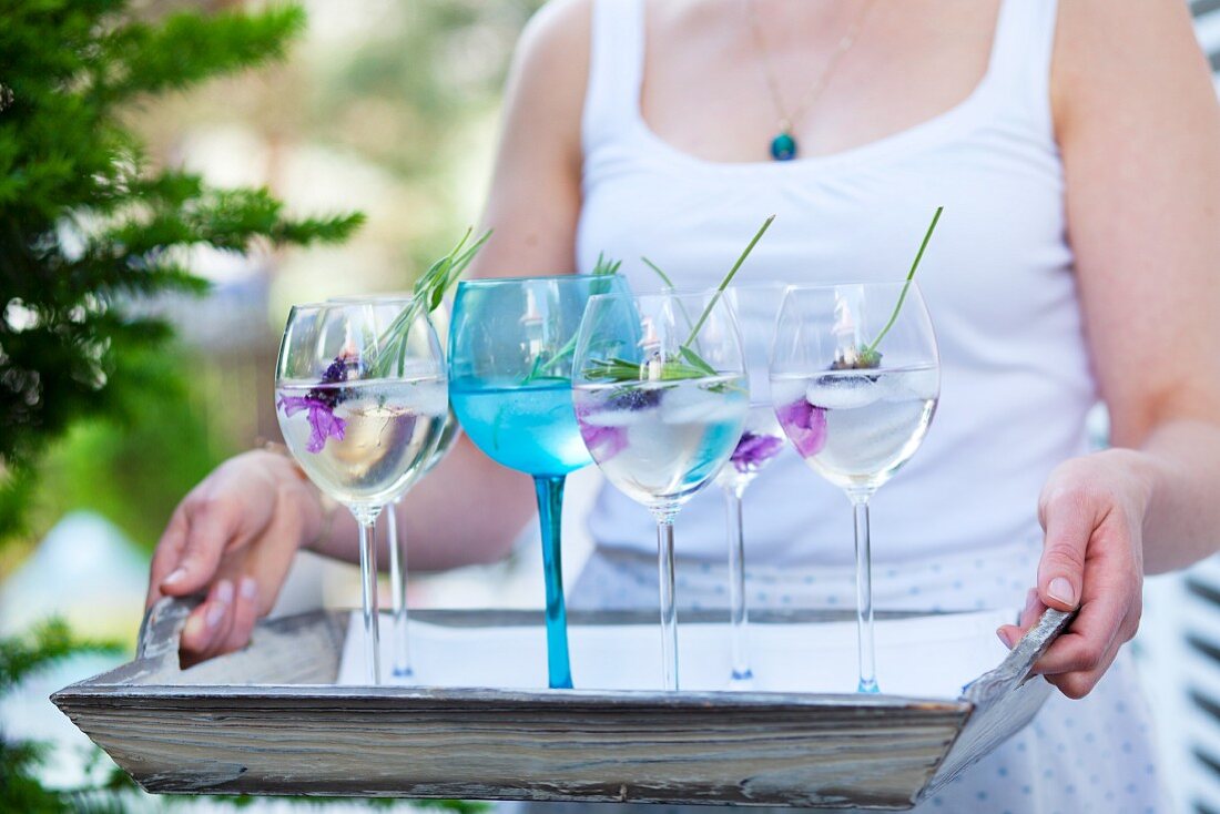 Frau hält Tablett mit mehreren Gläsern Lavendelwasser