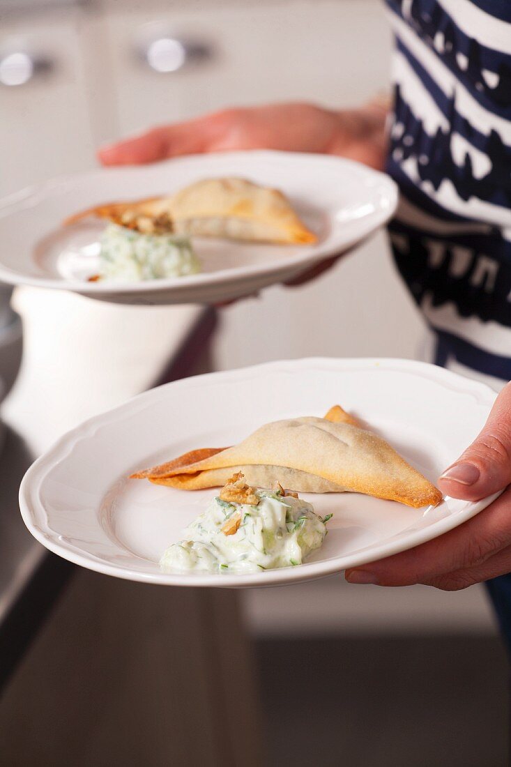 Frau serviert gefüllte Teigtaschen mit Gurkensalat (Polen)