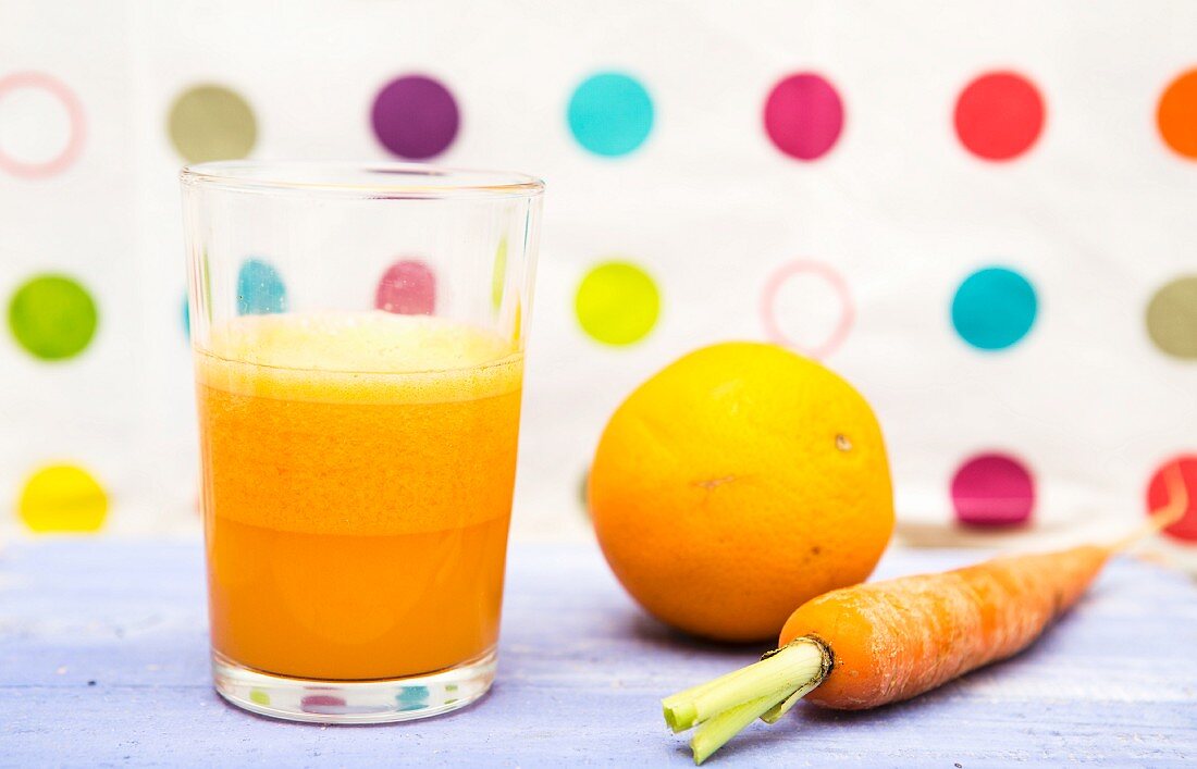 Ein Glas Möhren-Orangen-Saft neben frischer Orange und Möhre