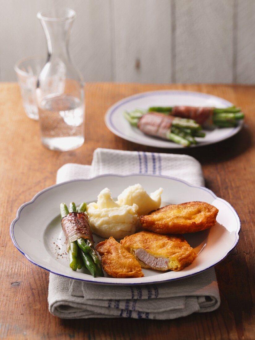 Breaded pork schnitzel with mashed potatoes and green beans wrapped with bacon