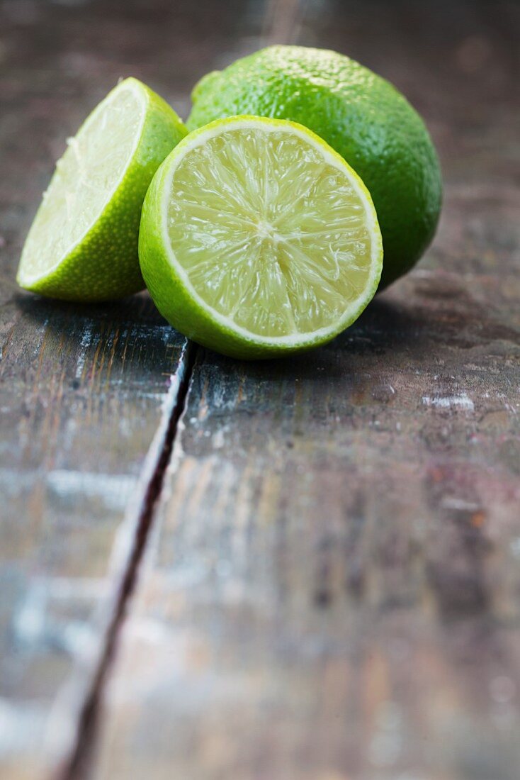 Two lime halves and a whole lime on a wooden surface