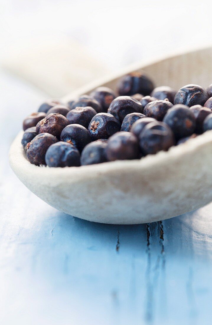 Getrocknete Wacholderbeeren in einem tiefen Holzlöffel auf blauem Holzuntergrund