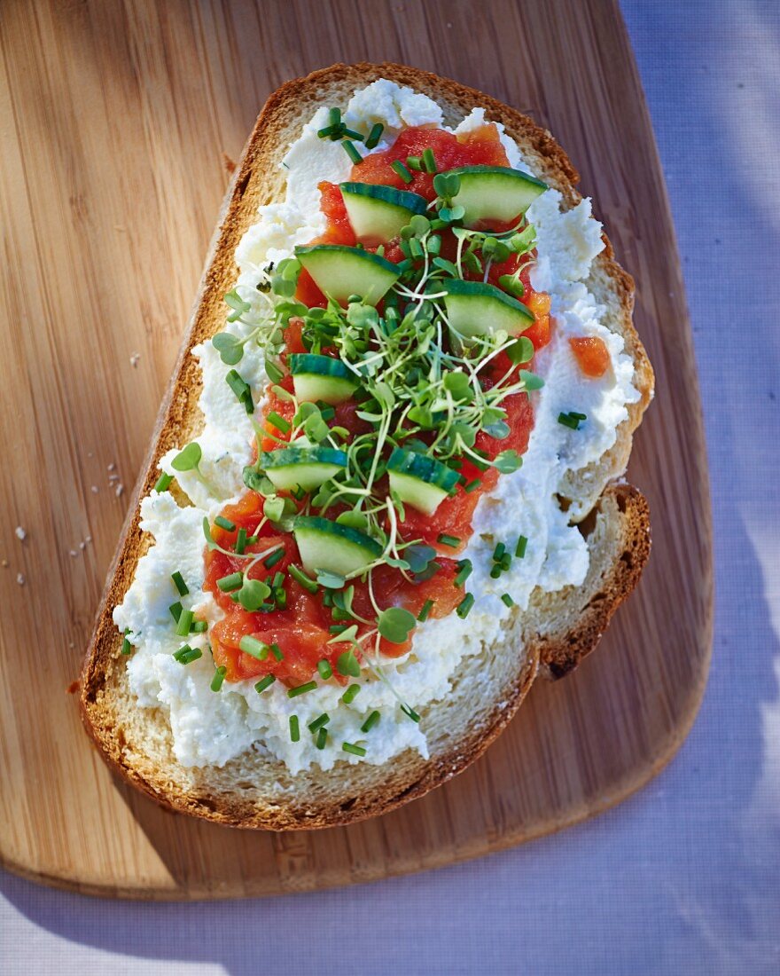 A slice of bread topped with goat's cheese, tomatoes, cucumber and cress