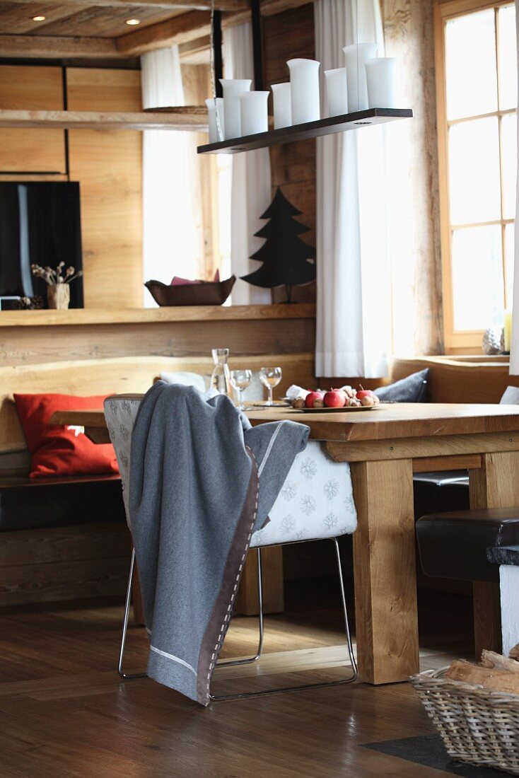 Blanket with decorative stitching on armchair at dining table below candles on suspended board