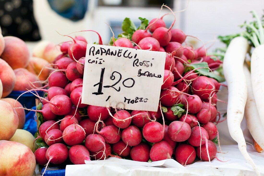 A pile of radishes at the market with a price sign