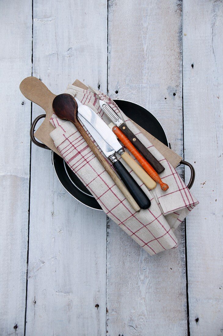 Cutlery, kitchen utensils, a tea towel and a chopping board, on top of a pan