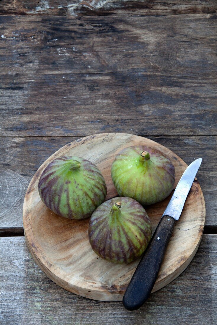 Three fresh figs on a round wooden board with a knife