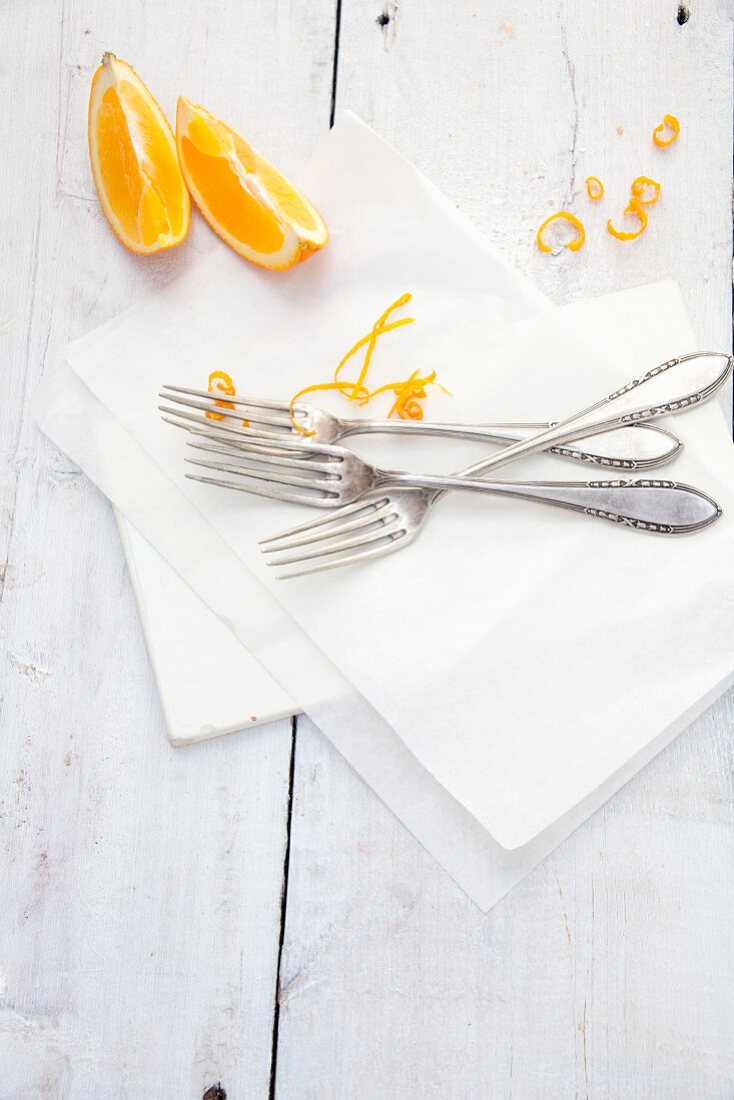 Orange wedges, orange zest and forks on baking parchment