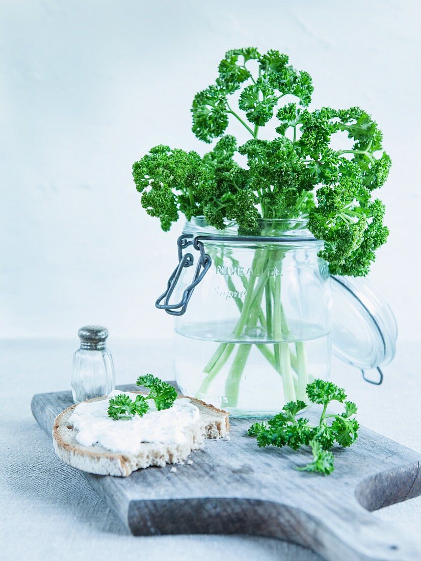 Curly-leaf parsley in a storage jar, a slice of rustic bread with herb quark and fresh parsley