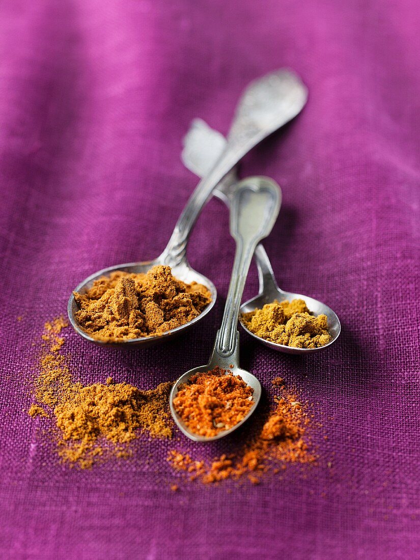 Assorted types of curry powder on old silver spoons on purple material